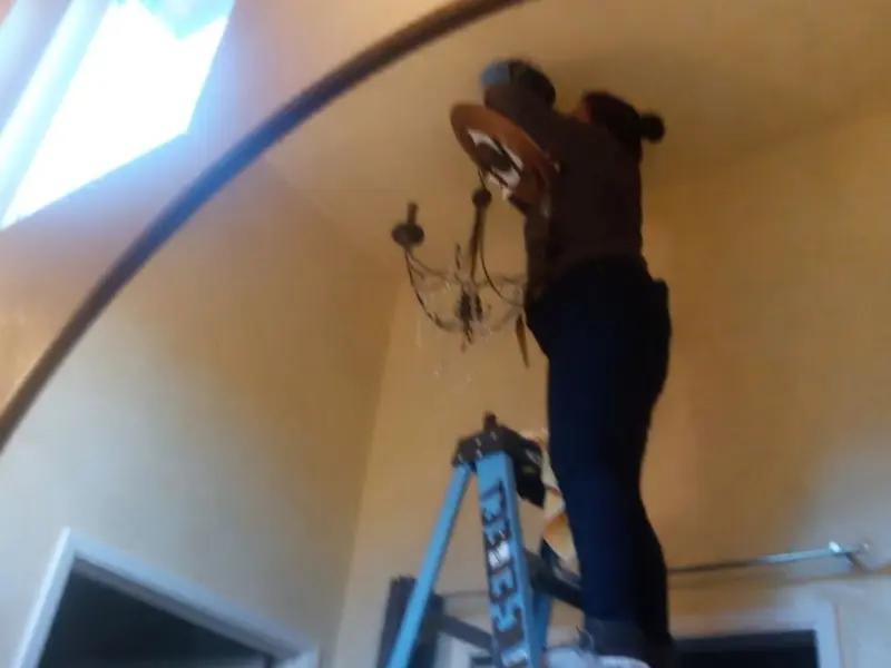 Electrician installing a chandelier in a Howland Center residence